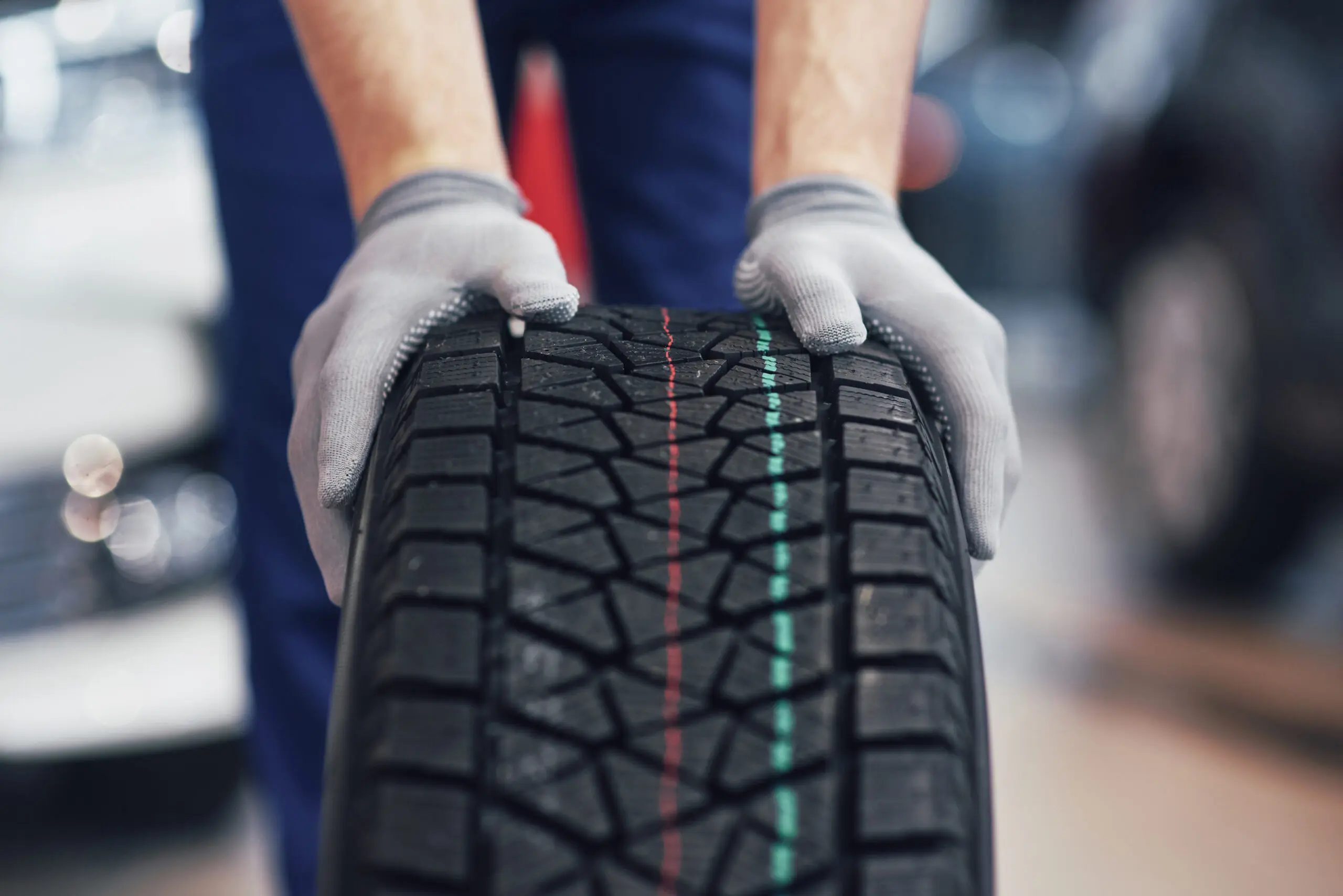 Closeup of mechanic hands pushing a black tire in the workshop. Closeup picture of a mechanic with gloves rolling a tire