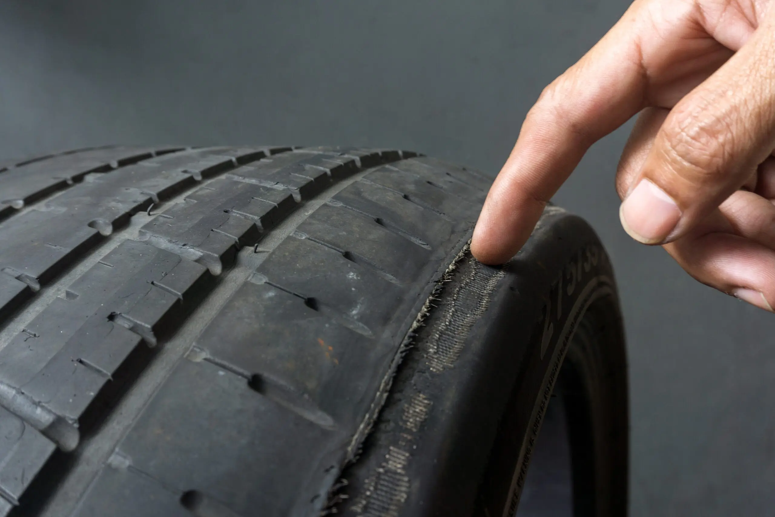 Finger pointing to damage on tire tread. Tire tread problems by improper tire pressure, Wheel alignment