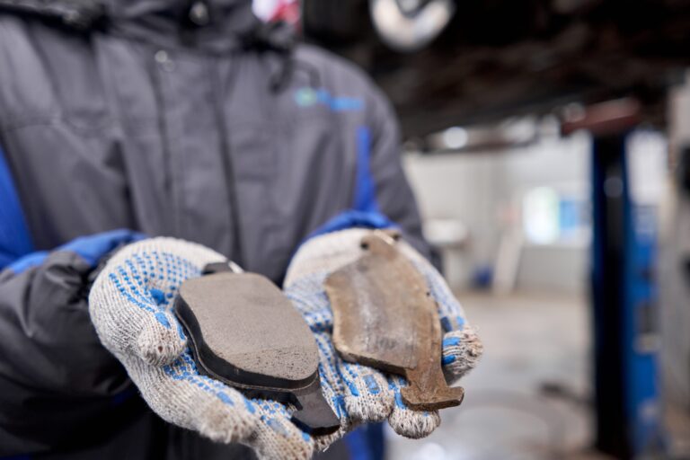 The mechanic holds the old and new brake pads in his hand. Change the old to new brake disc on car in a garage. Auto repair concept.