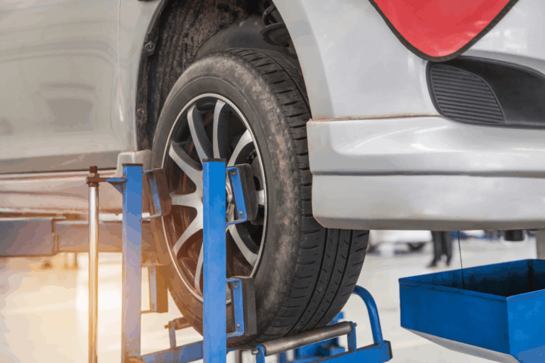 A vehicle lifted up in a shop with a jack holding one of the tires in place.