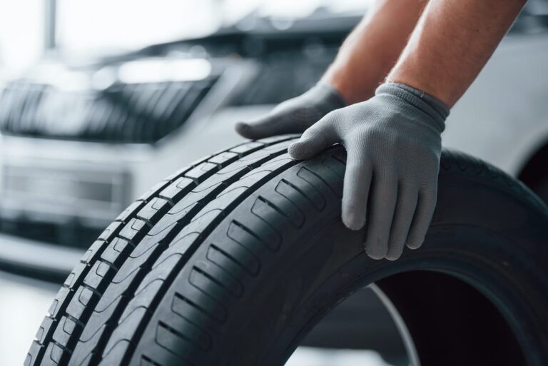 Mechanic pushing black tire with gloved hands.