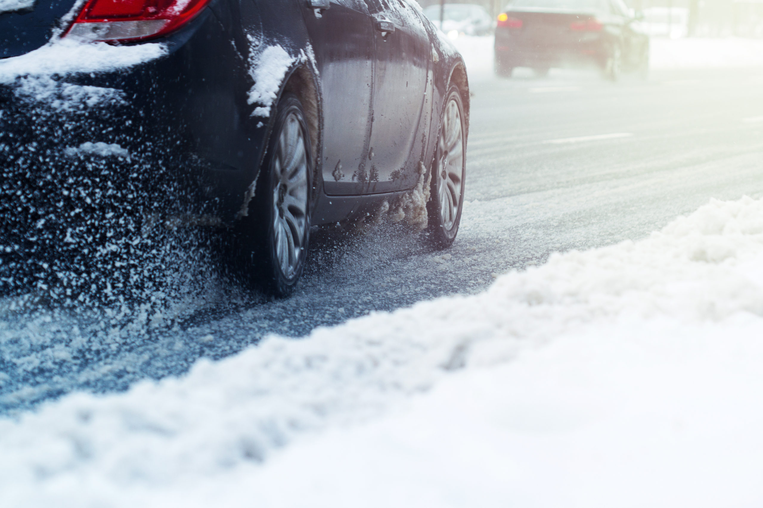 closeup rear view of a car dark color wheel tire going through snow on a city road traffic with motion blur