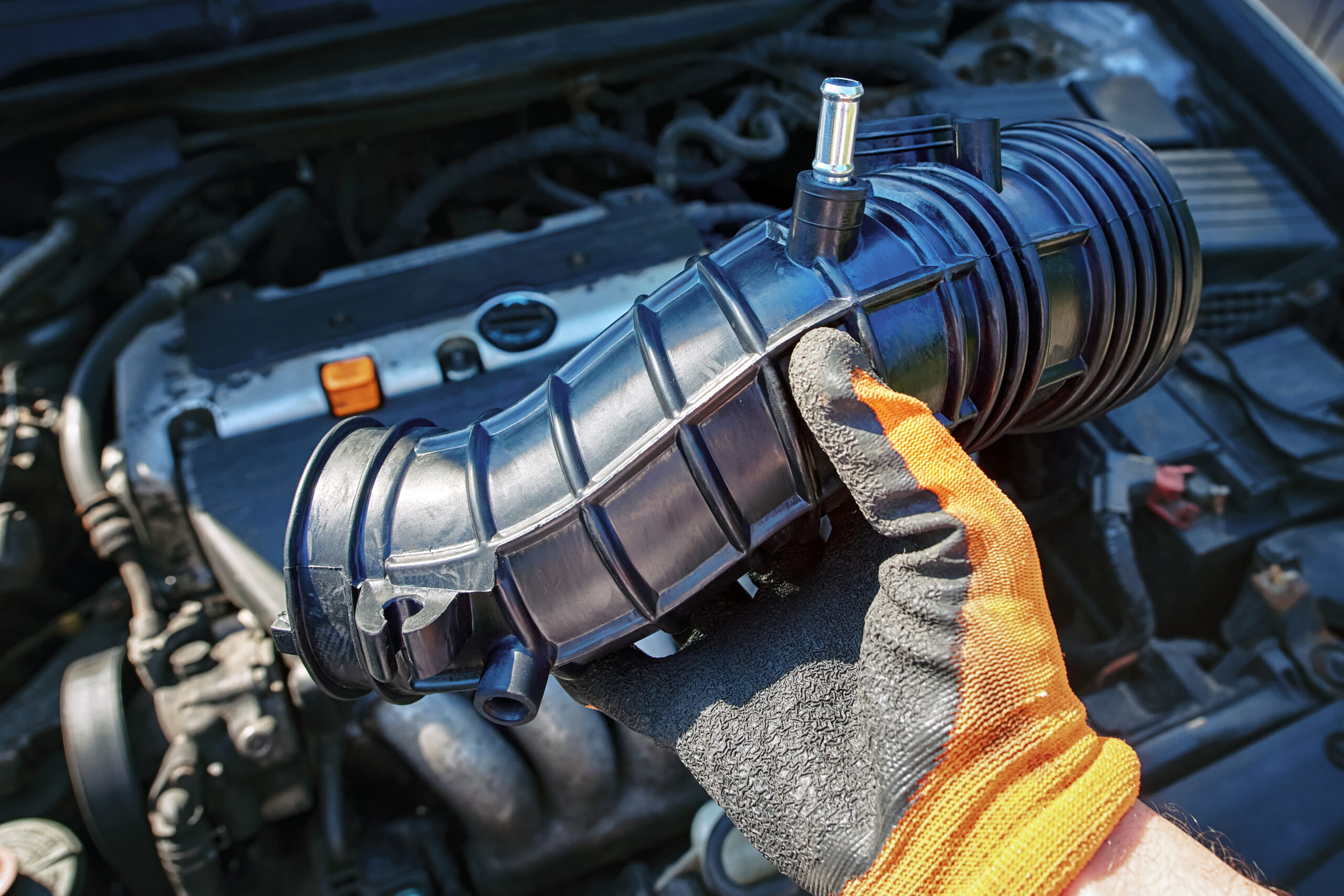 Mechanic holding an air intake hose with a car engine in the background.