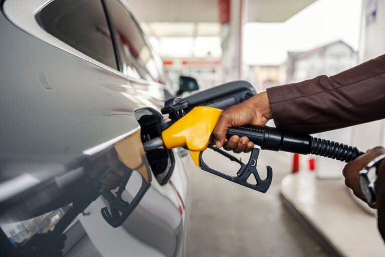 Cropped picture of a man's hand holding nozzle and filling up the tank at gas station.