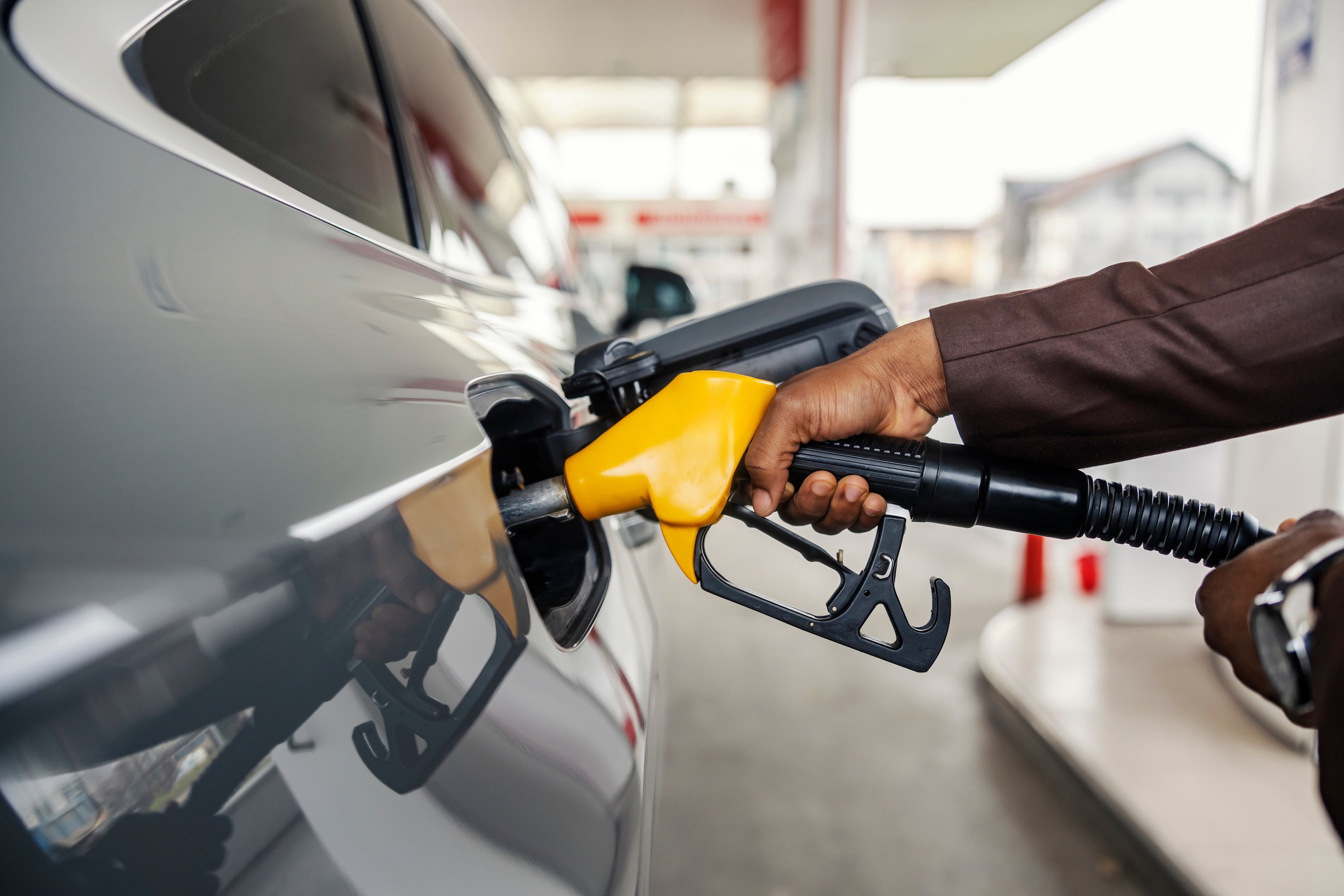 Cropped picture of a man's hand holding nozzle and filling up the tank at gas station.