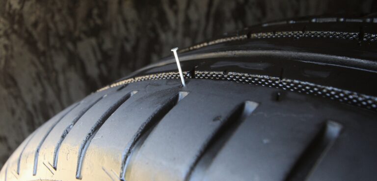 Close up of a run-flat tire with a metal nail sticking out from the tread.