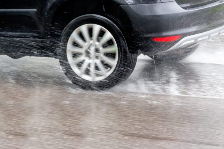 Dark grey vehicle driving on very wet road, spraying water up and trying not to hydroplane.