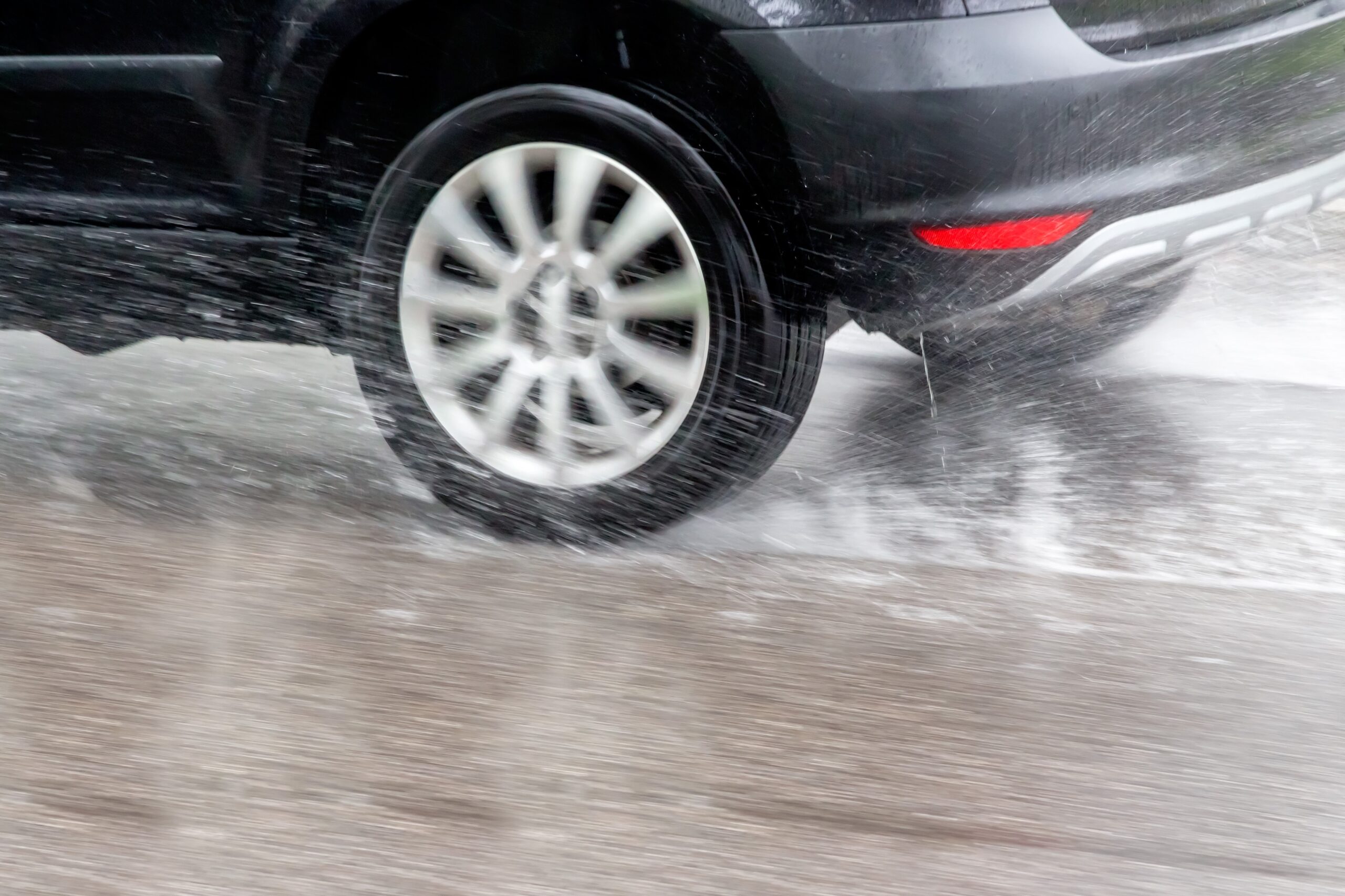 Dark grey vehicle driving on very wet road, spraying water up and trying not to hydroplane.