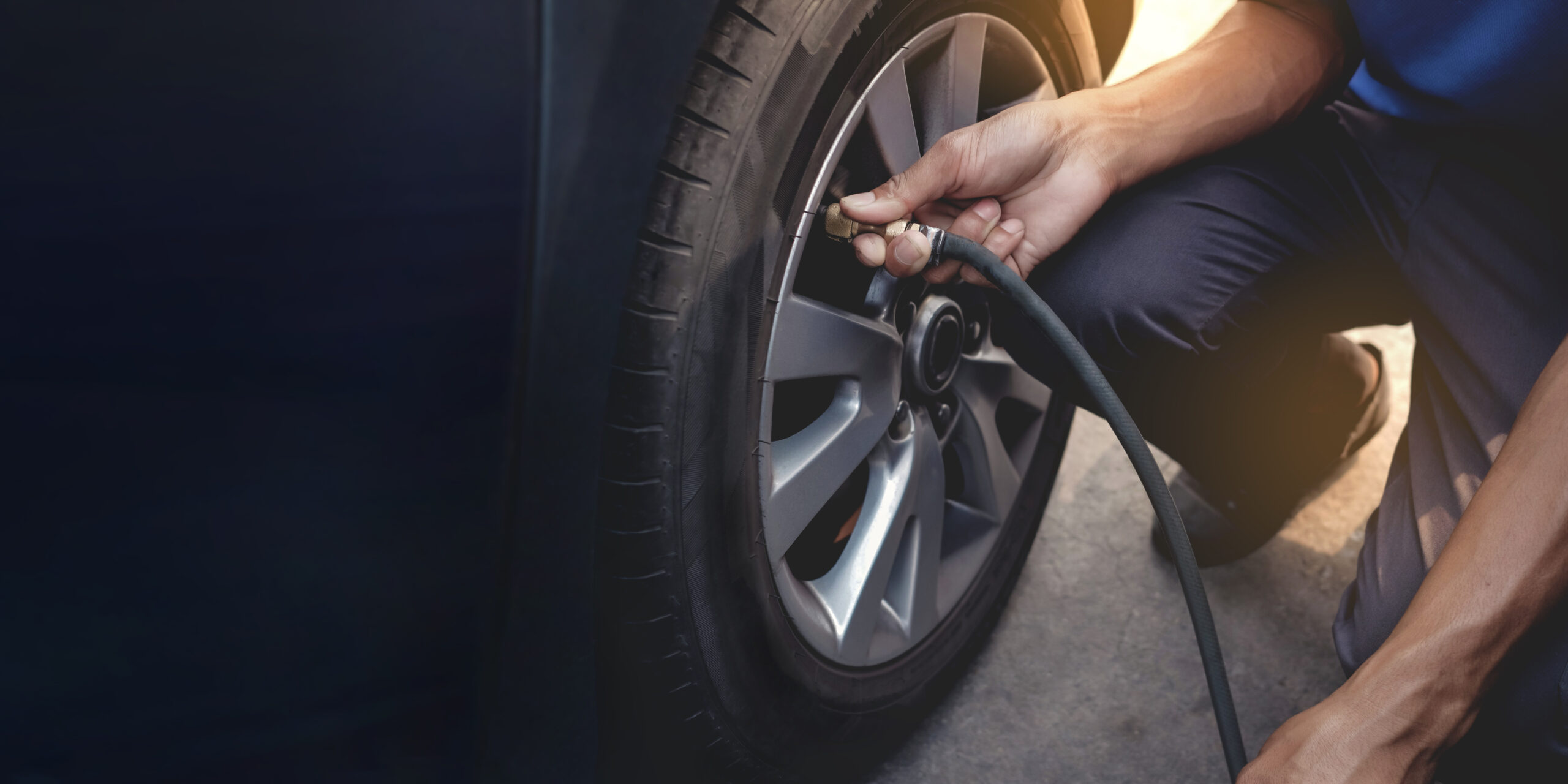 A closeup of a person adding air to his vehicle tire using a small air hose hooked to the tire's air valve.