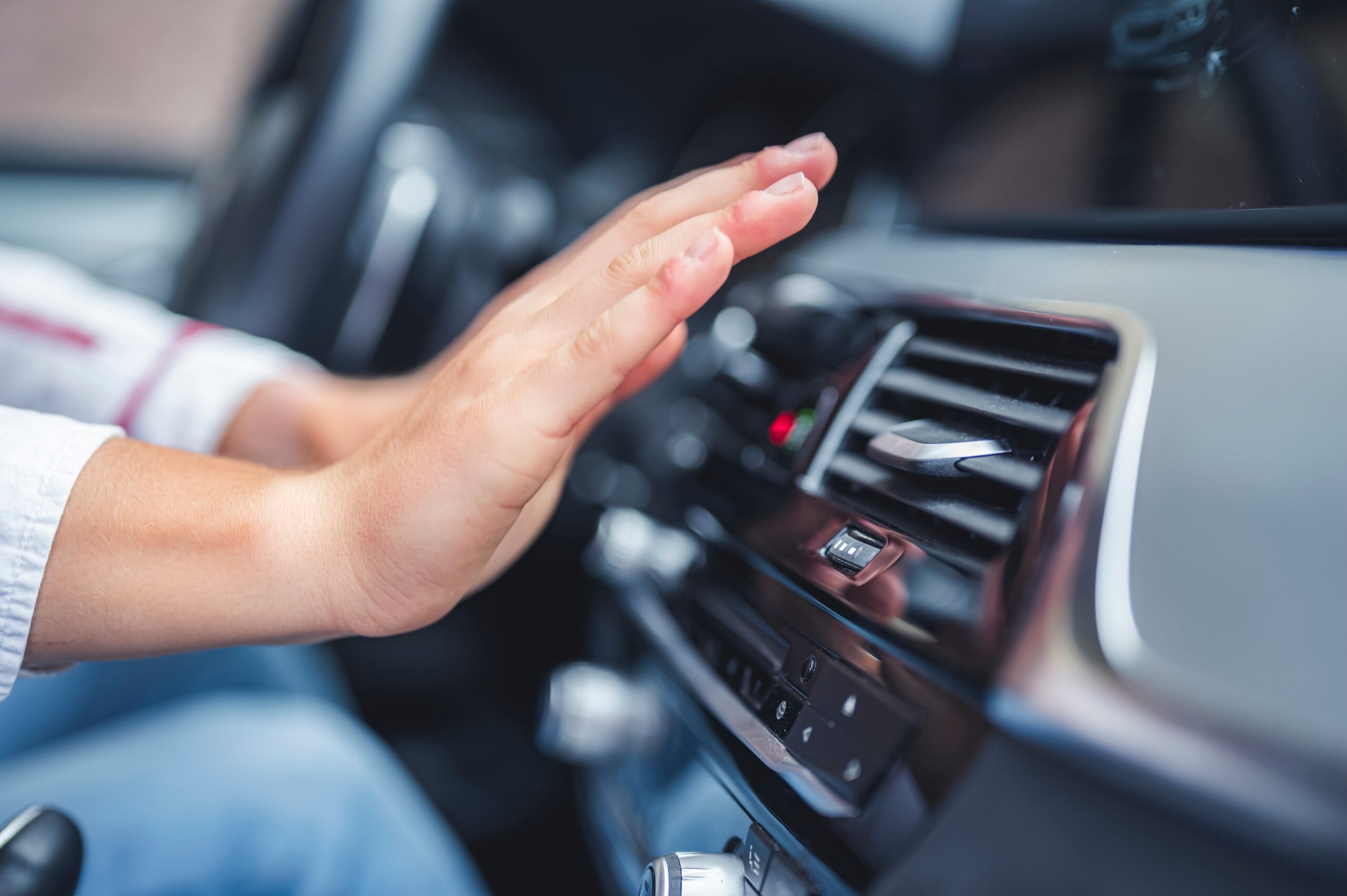 Person checking the air conditioner and cooling system in the car with their hand in front of the air vent.
