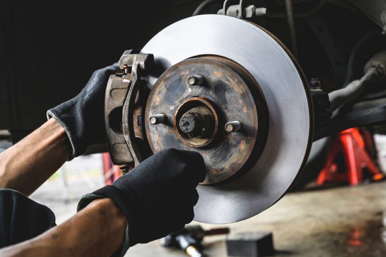 Mechanic installing front brake caliper and brake pads on vehicle.