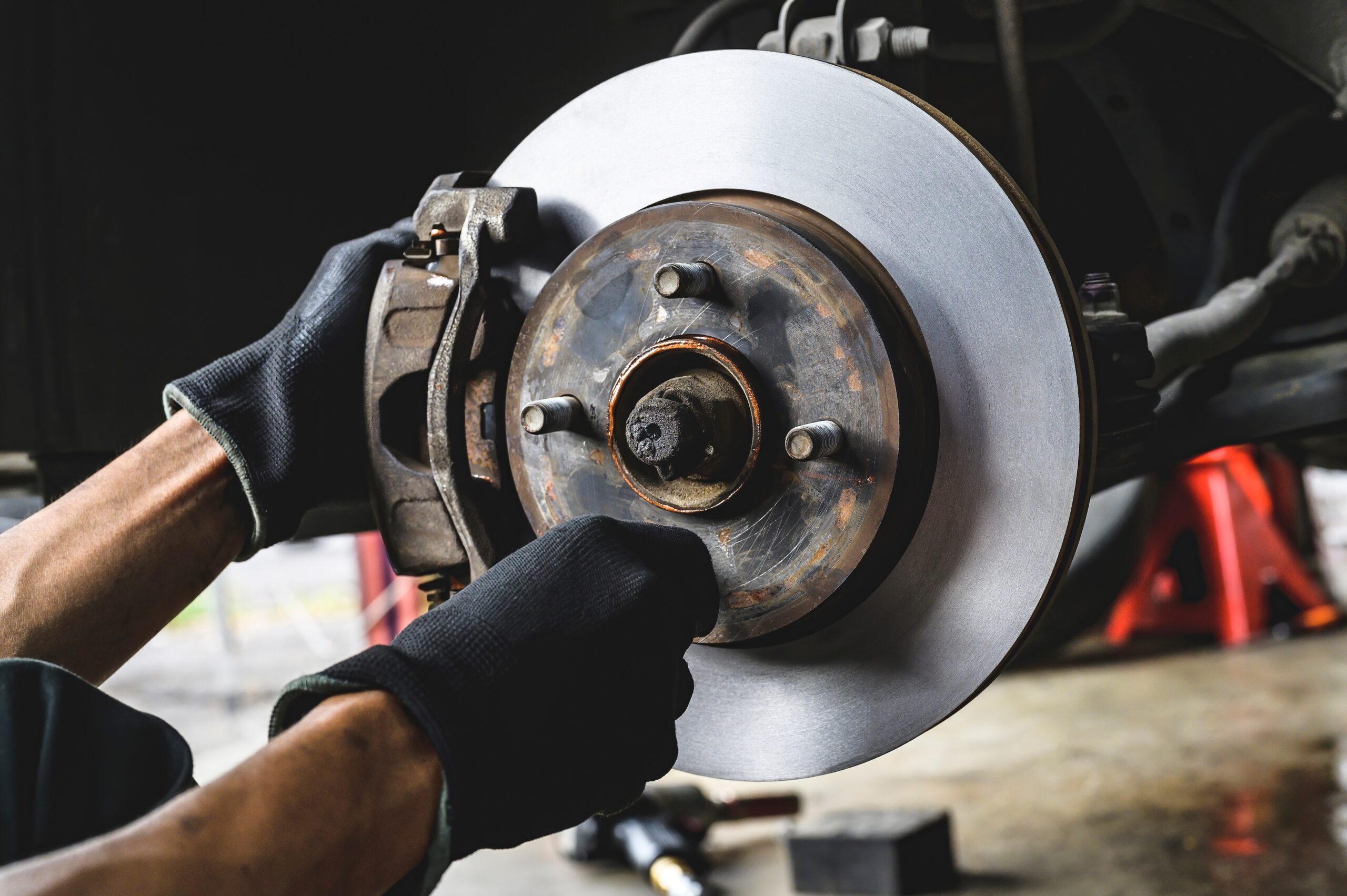Mechanic installing front brake caliper and brake pads on vehicle.