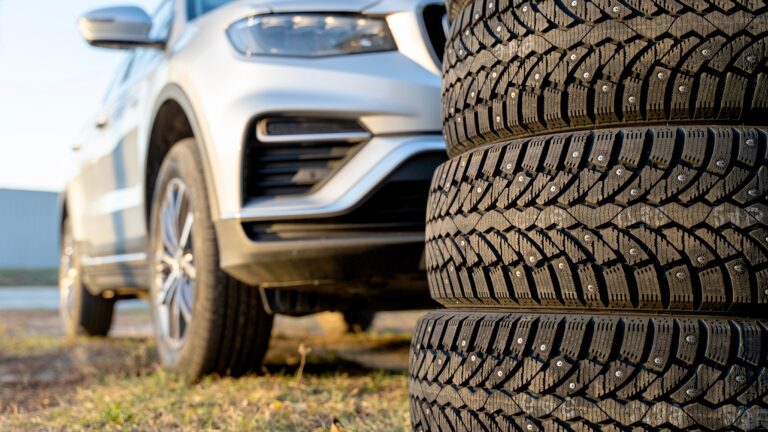 A stack of winter tires in front of a parked vehicle, ready to be installed before winter weather hits.
