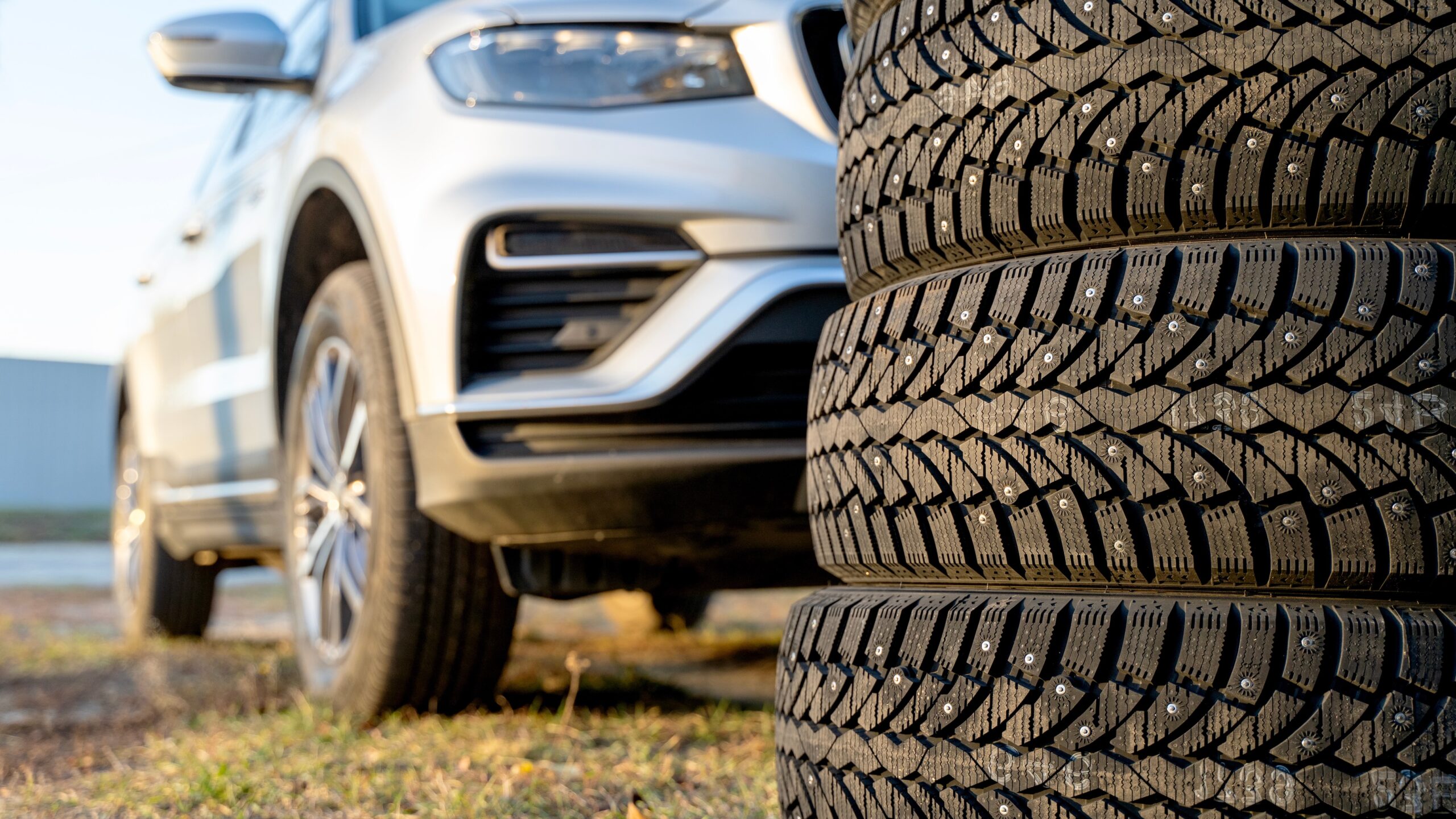 A stack of winter tires in front of a parked vehicle, ready to be installed before winter weather hits.