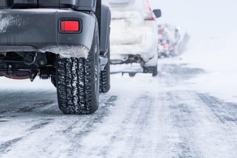 Cars on a snowy road with tires covered in snow during winter driving conditions.