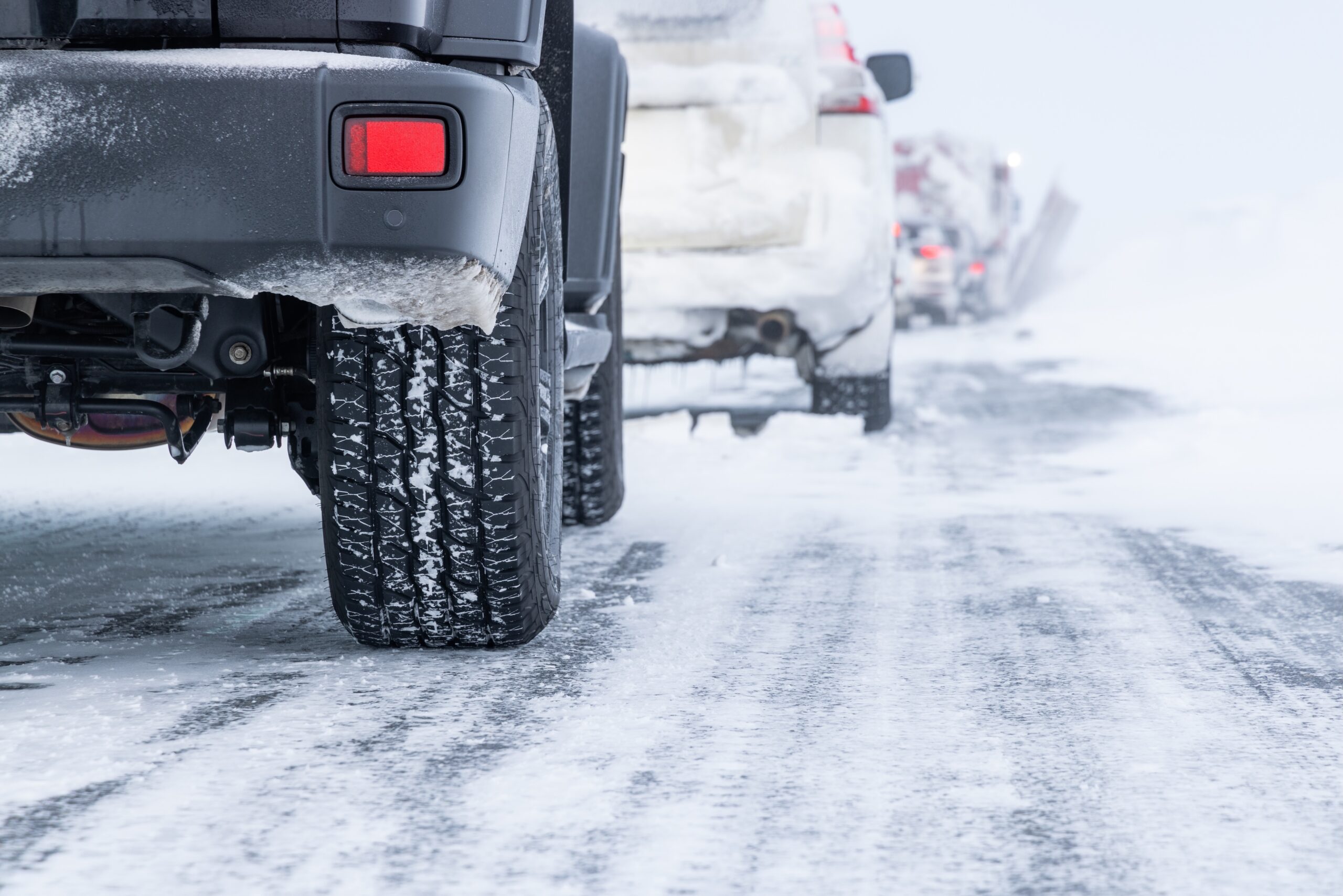 Cars on a snowy road with tires covered in snow during winter driving conditions.