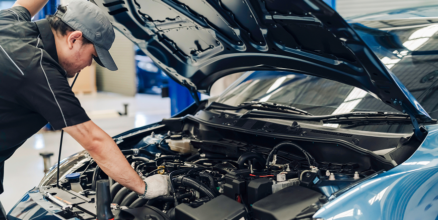 A Telle Tire automotive technician working on a car engine with the hood up.