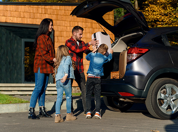 A mother, father, and two young children working together to put luggage into the trunk of their small SUV.